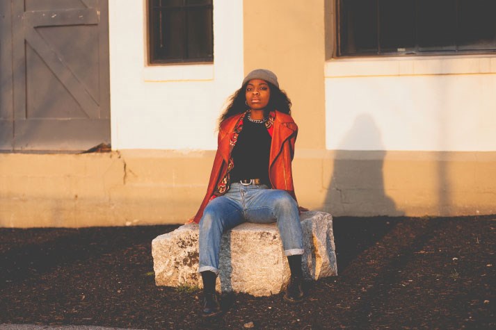 Brittany Tsewole sits on a granite block outside a building with barn door