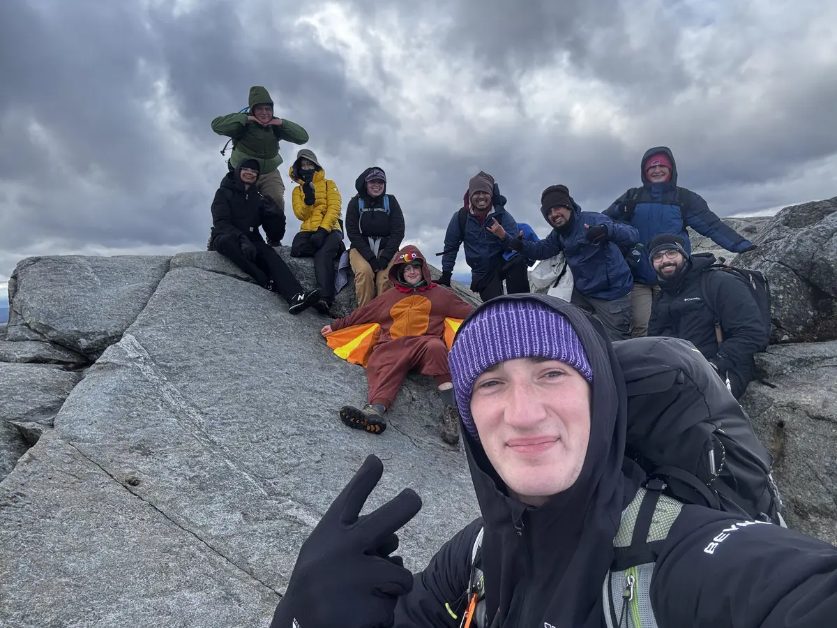 A group smiles at the top of a rocky summit; one person is wearing a turkey costume.