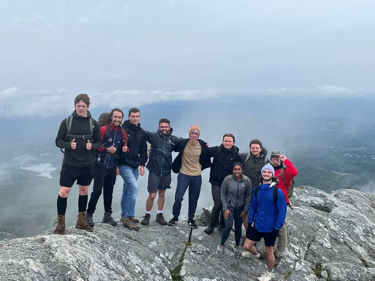a group of hikers stands atop a rocky summit with the valley below shrouded in clouds
