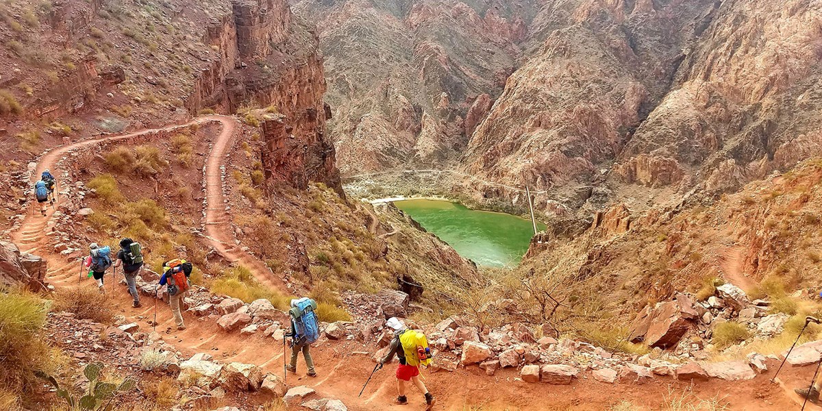 A wide shot of a beautiful canyon with hikers walking along a trail through it.