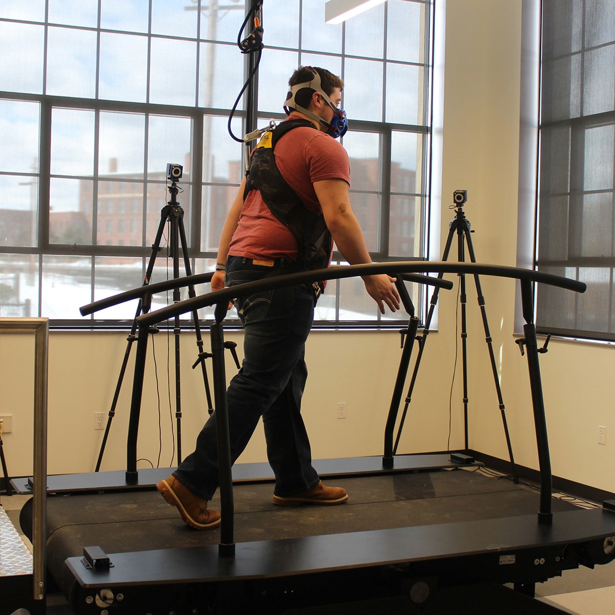 A person wearing a portable VO2 measurement device walking on an instrumented treadmill with motion capture cameras.