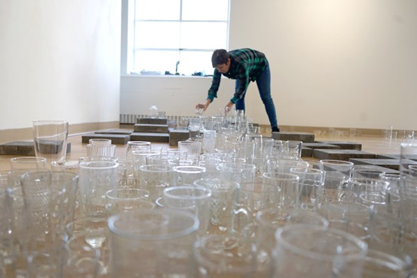 Evelyn Rydz arranges thrifted glassware into a symbolic Merrimack River for her part of the current Local Ecologies exhibit in Moloney Gallery.