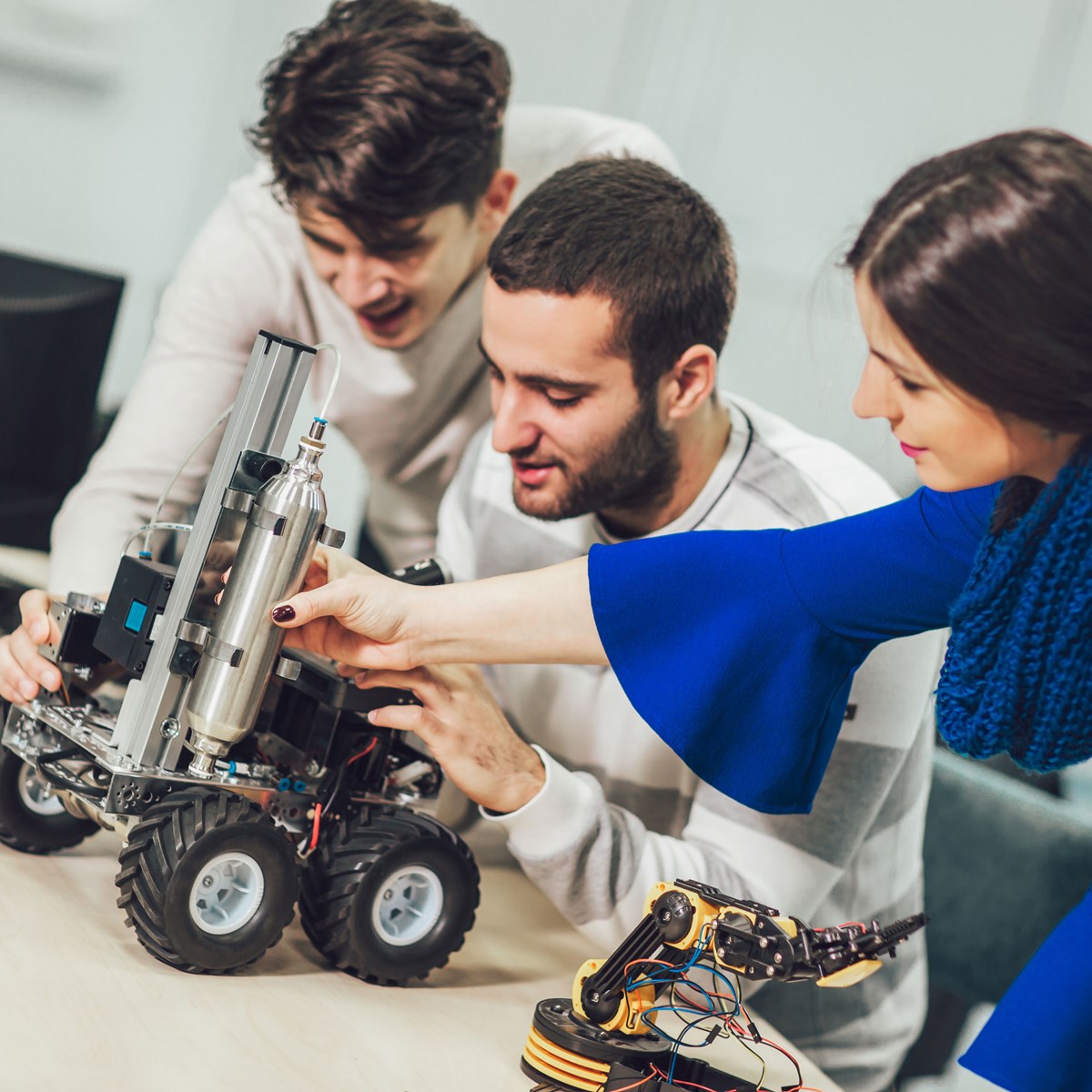 Three industrial engineering students working on and looking at a robotic device