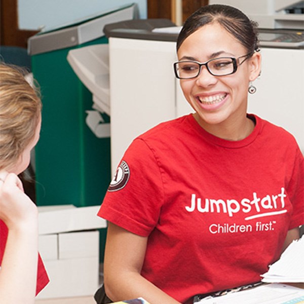 Young woman with glasses smiles while wearing a red Jumpstart T-shirt