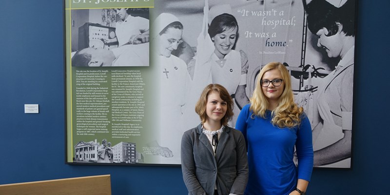 Kady Phelps with Kim Cosgrove in front of an exhibit they recently completed about St. Joseph’s Hospital, which was located where University Crossing now stands
