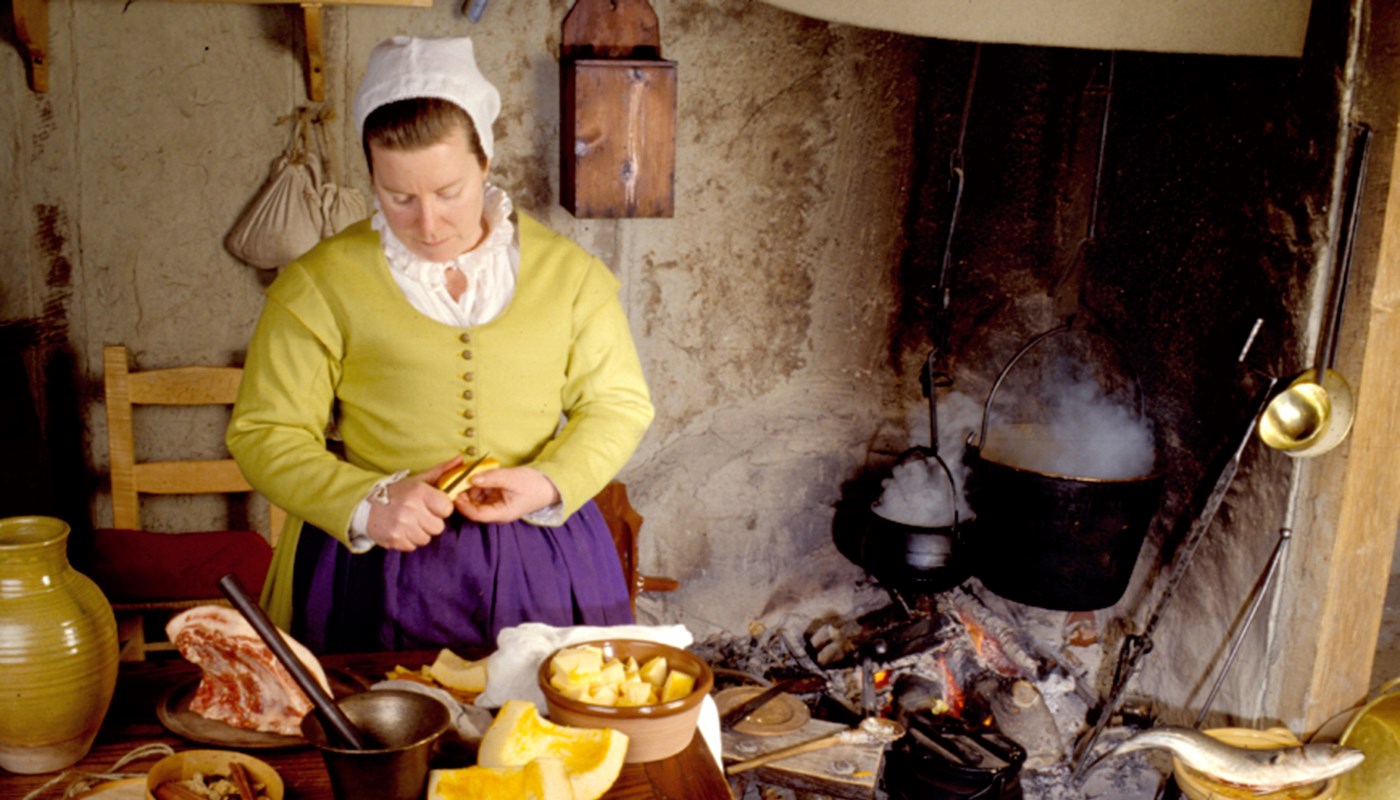 Kathleen Curtin dressed as a colonist preparing food at Plimoth Plantation