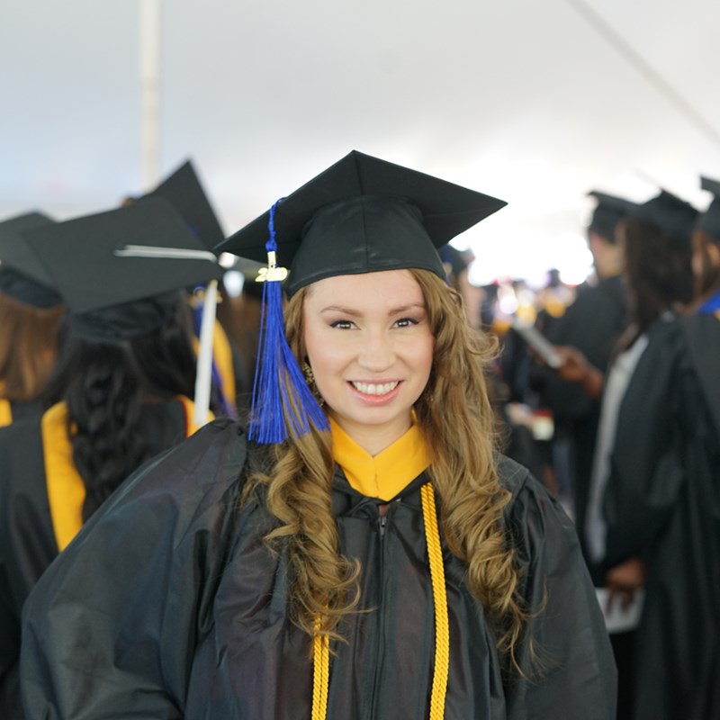 Headshot of Kendra Cervantes in a cap in gown outside of the Tsongas Center at UMass Lowell at Commencement 2019
