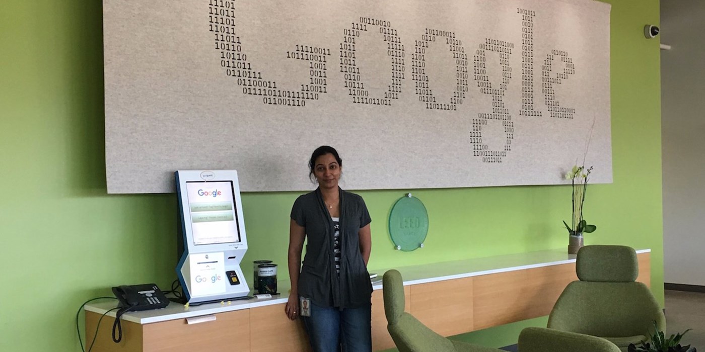 Kripa Krishnan stands in front of a big sign that reads "Google" in 1s and 0s