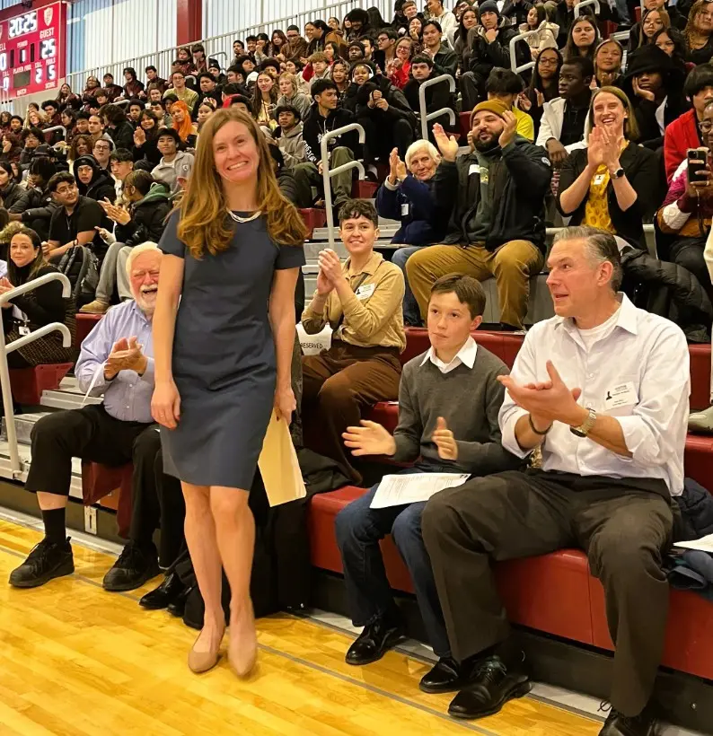 Lara Goodhue stands and accept applause from a gymnasium full of students and teachers