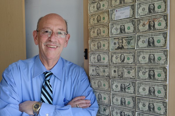 Larry Siegel poses with a collection of three neat columns of dollar bills, $5 bills and a couple of higher denominations—in all, 41 bills totaling $134— mounted on the back of a cabinet door