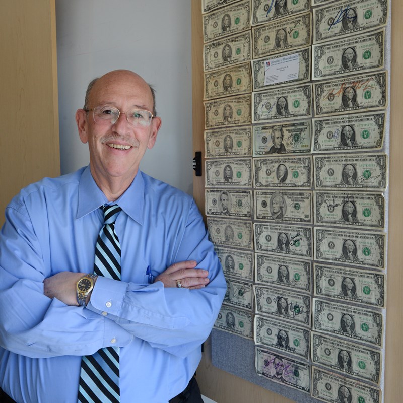 Larry Siegel stands in front of a bulletin board covered in $1 bills