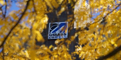 UMass Lowell logo on building seen through yellow tree leaves
