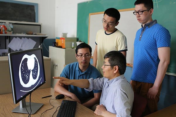 Research team led by Assoc. Prof. Hengyong Yu gathered around computer screen.