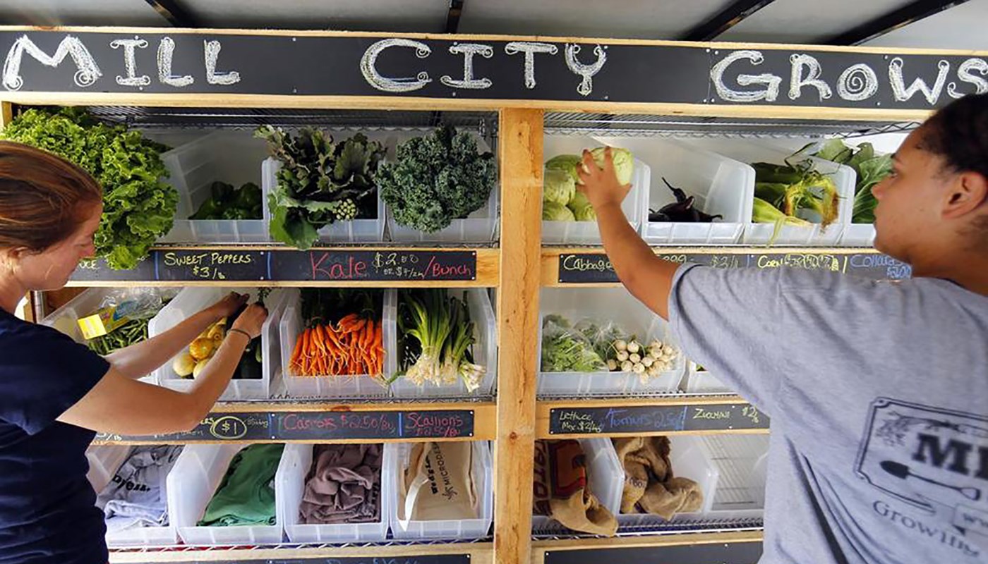 Lydia Sisson and another woman stock a Mill City Grows vegetable stand at a farmer's market