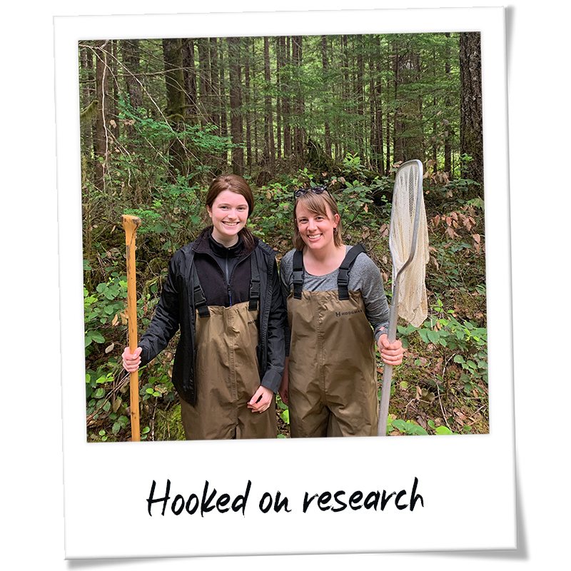"Polaroid" photo of Maeve Moynihan working with Asst. Prof. Natalie Steinel wearing fishing gear and holding nets - handwriting on photo frame reads "Hooked on research"