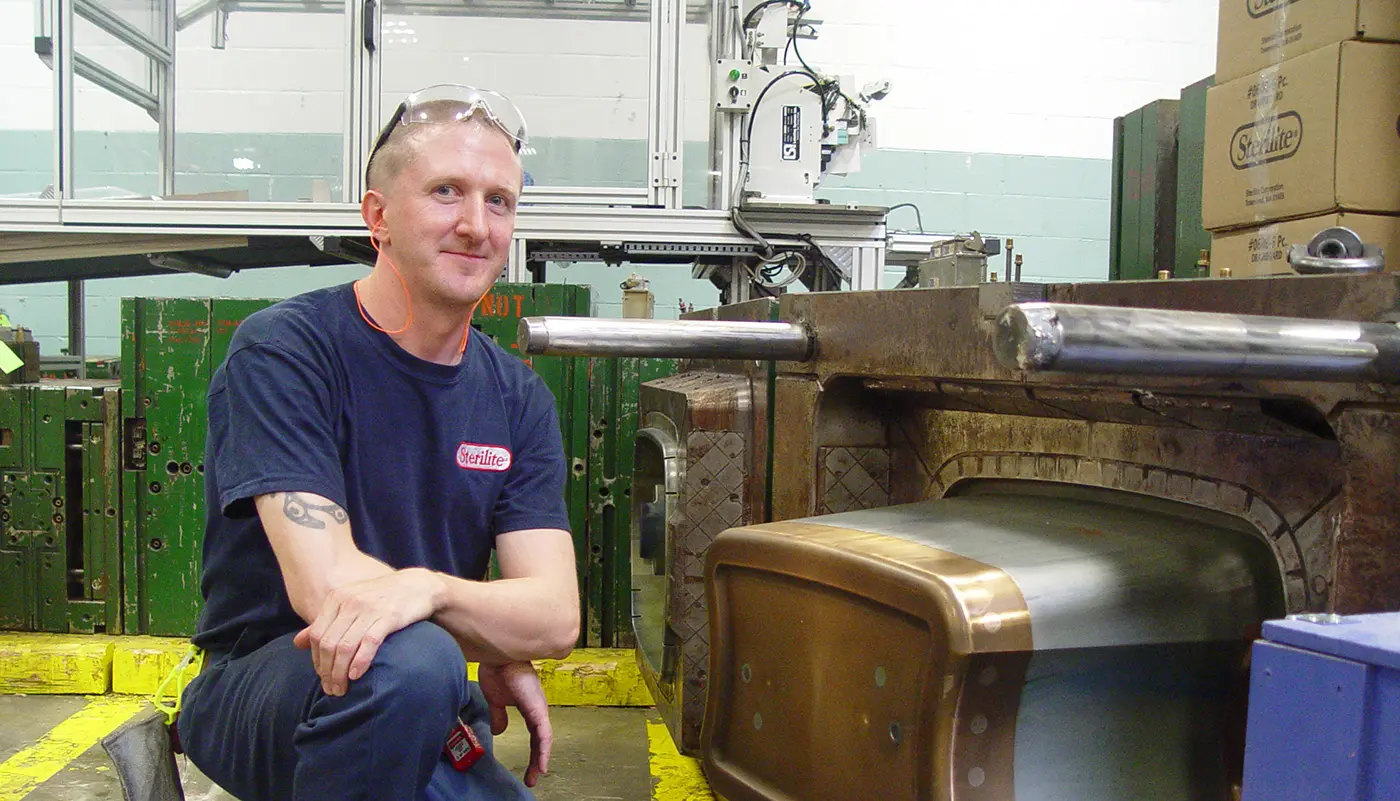 A male UMass Lowell student poses next to a piece of machinery on her co-op at Sterilite.