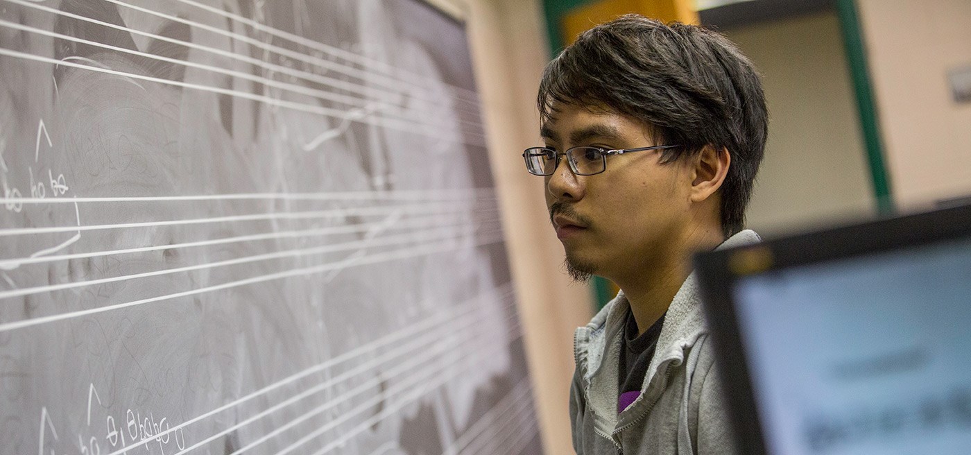 A male student writing music/composing on a chalk board.