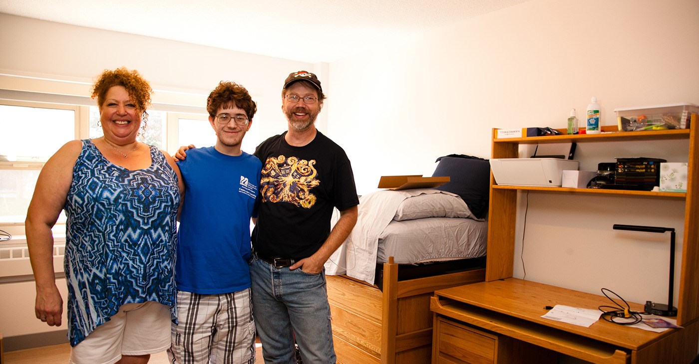 male-student-poses-with-parents-in-room