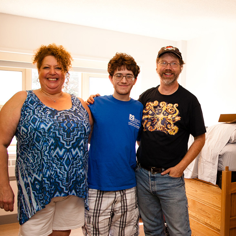 A male student poses with his parents in his room