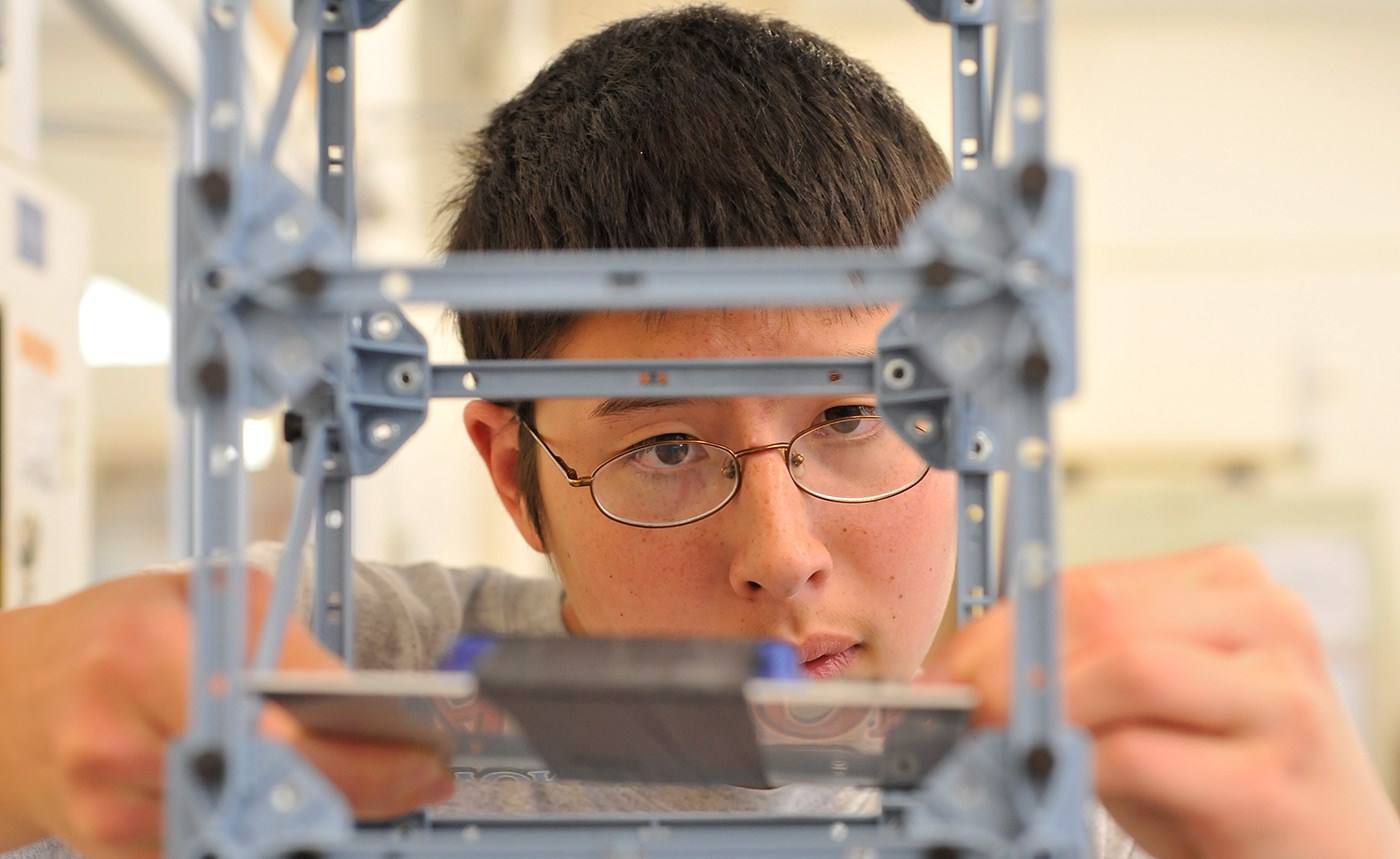 A male UMass Lowell student seen through the other side of his bridge model.