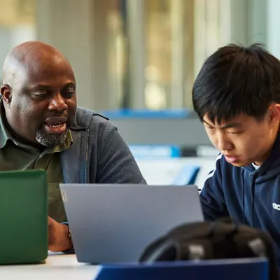 Man talks to student while both look at laptops