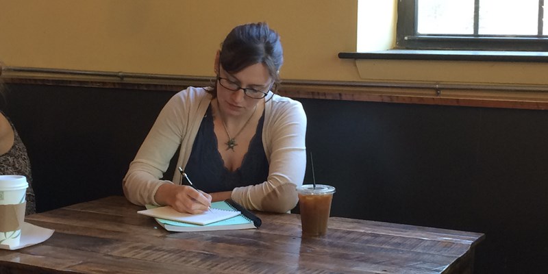 Mary Everett writes in a notebook at a table at a cafe