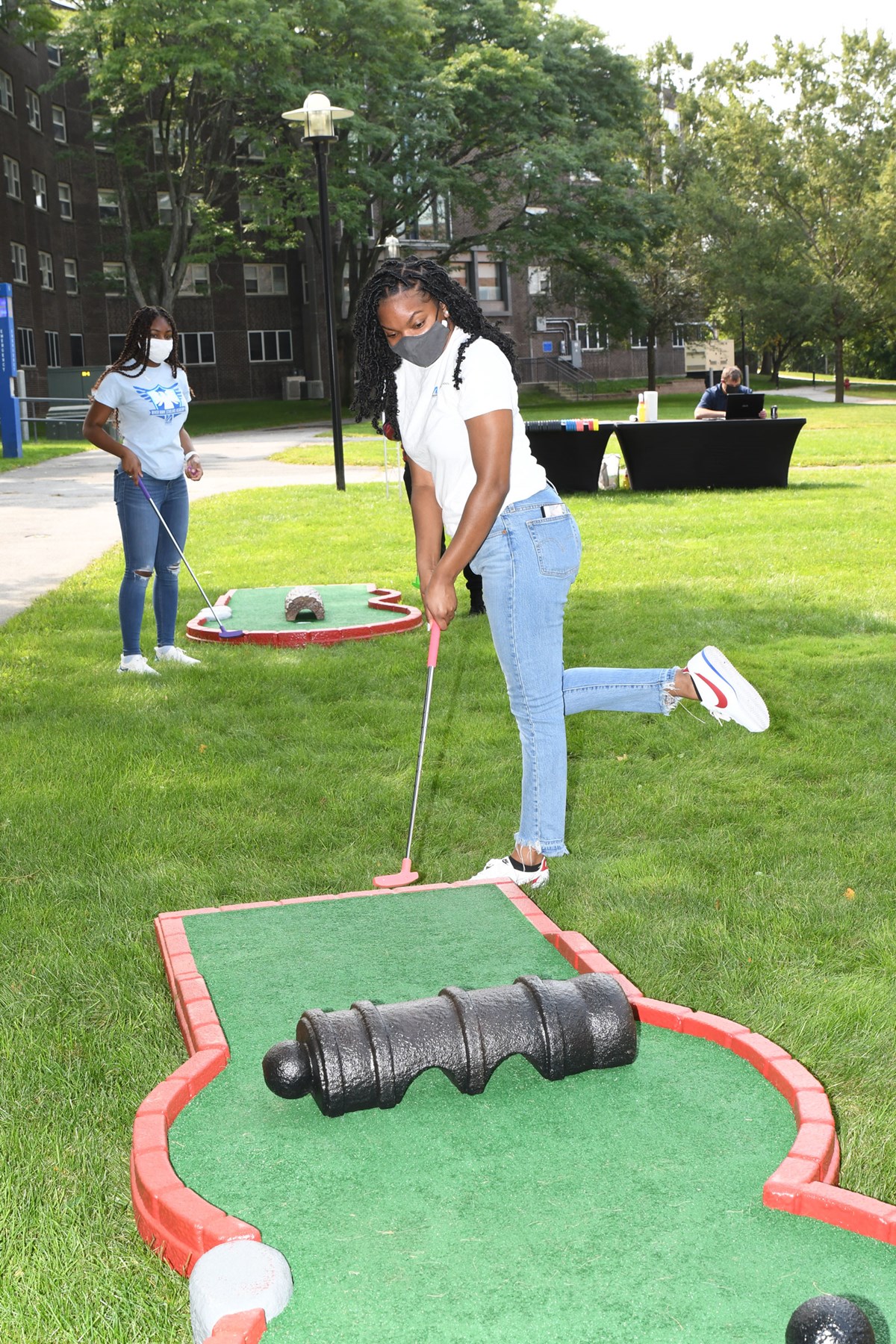 woman with mask plays mini golf on res hall lawn