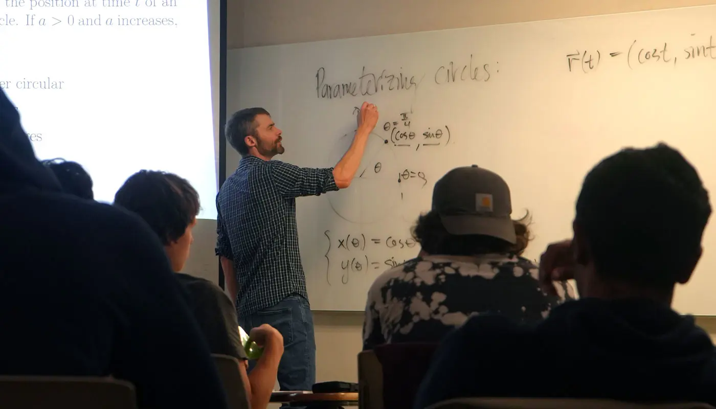 Math professor writes equations on a whiteboard in a UMass Lowell classroom.
