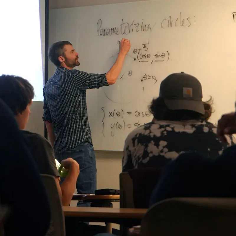 Math professor writes equations on a whiteboard in a UMass Lowell classroom.