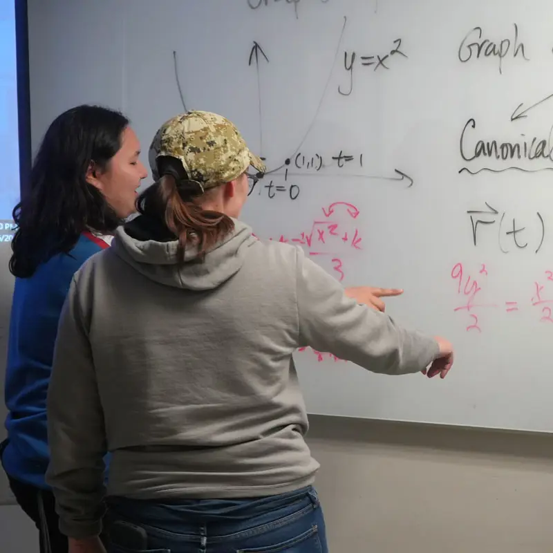 Two students discuss math equations written on a whiteboard at UMass Lowell.