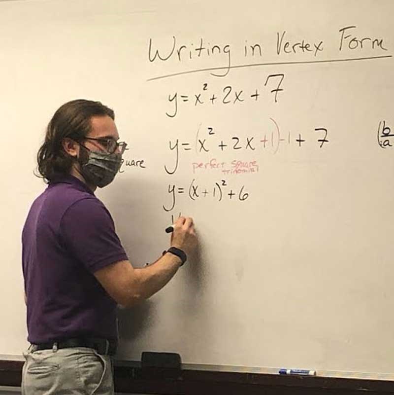 Math student wearing a mask writes formulas on a whiteboard