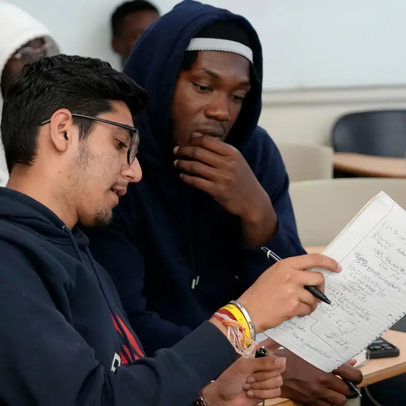 Two students discuss equations written in a notebook in a UMass Lowell math classroom.