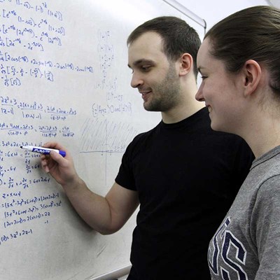 Two UMass Lowell math students write equations on a whiteboard