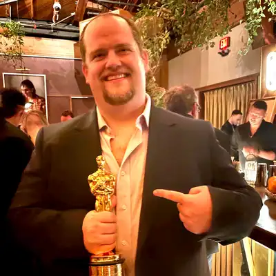 Six men in formal wear pose for a photo while one of them holds an Oscar trophy.
