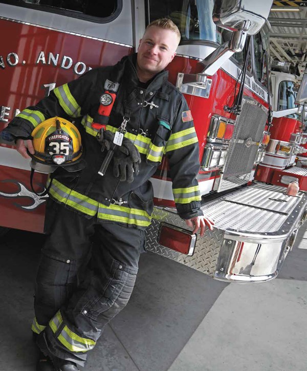 Matt Davis wearing fire gear holding his helmet in front of a fire truck