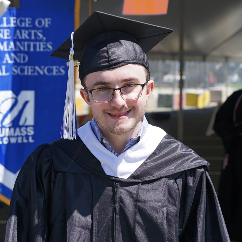 Headshot of Matthew Ferris in a cap in gown outside of the Tsongas Center at UMass Lowell at Commencement 2019