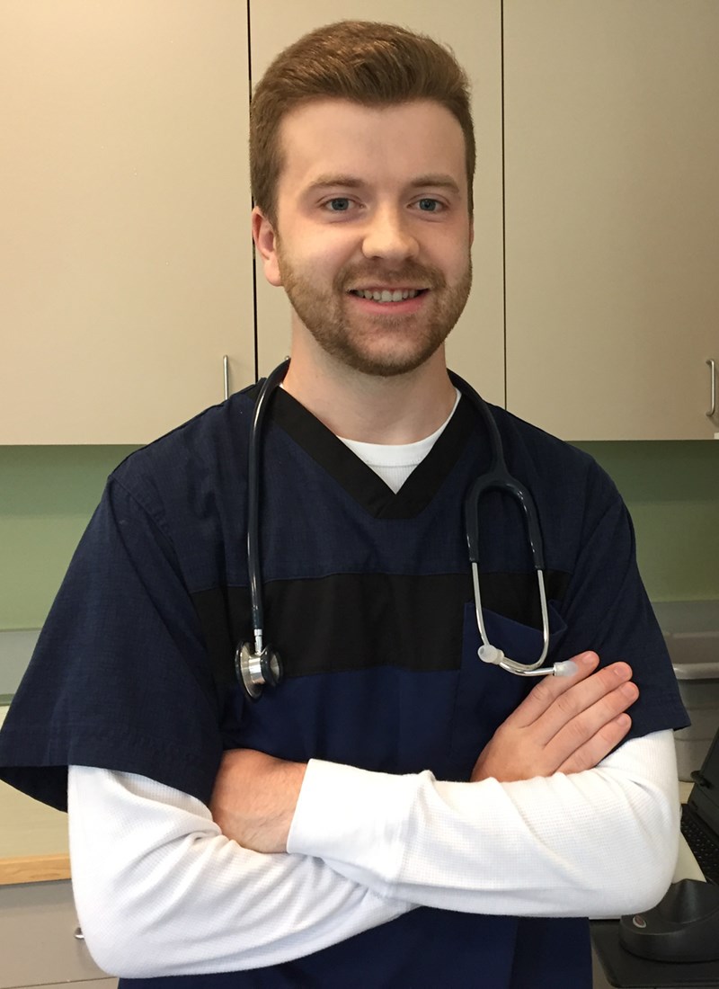 Matthew Fowler wearing scrubs and a stethoscope at a nursing simulation lab at UMass Lowell