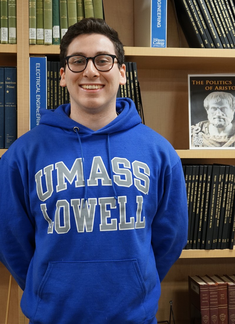 Head shot of Maxwell Aaronson in front of a bookcase wearing a UML sweatshirt