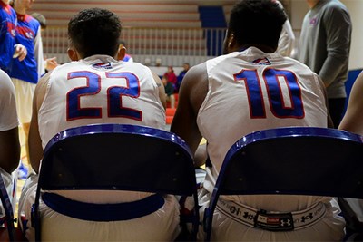 Backs of two men's basketball players sitting in chairs