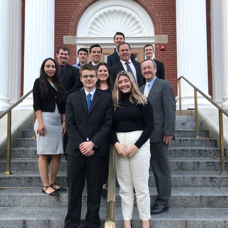 UML Mock Trial team poses on a set of stairs outside for a photo dressed professionally with Frank Talty