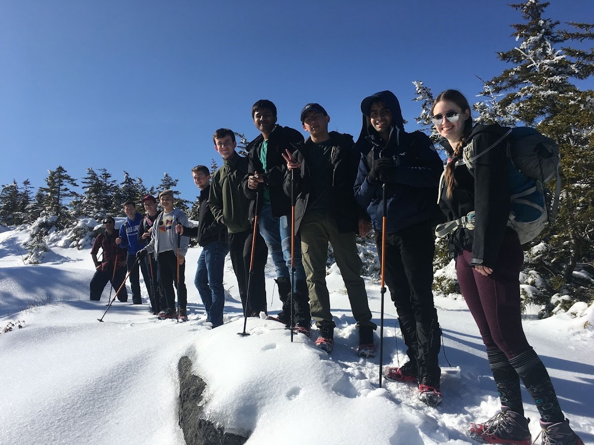 Students line up and smile near top of mountain with blue sky.