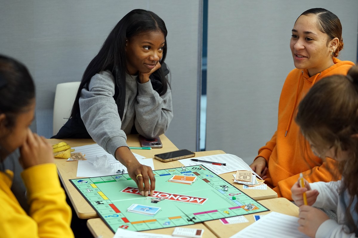 A young woman reaches for dice on a Monopoly board while looking at a player to her left