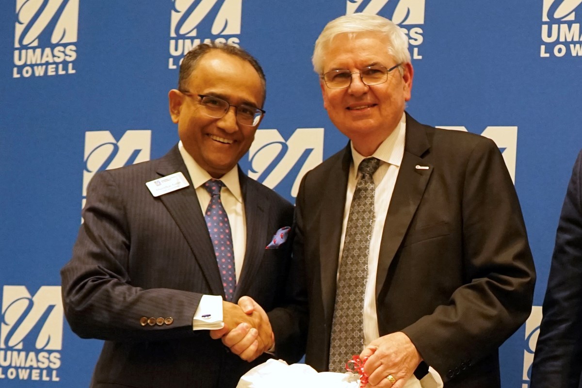 Two men in suits and glasses shake hands while posing for a photo