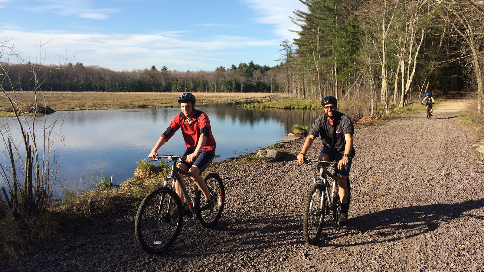 People riding mountain bikes in a wooded area next to a body of water.