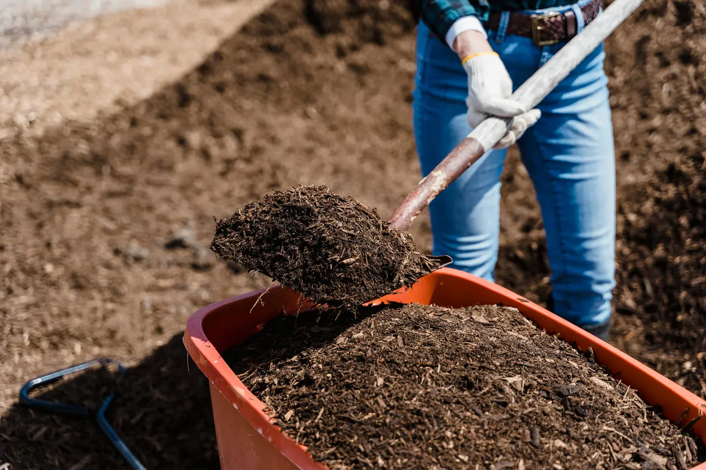 A person shovels mulch out of an orange container.
