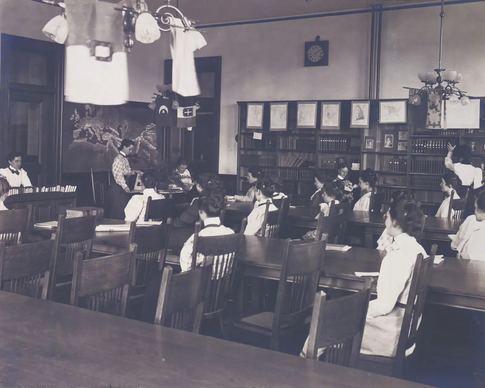 Black and white photo of women in high-collared blouses with their hair in buns in school library
