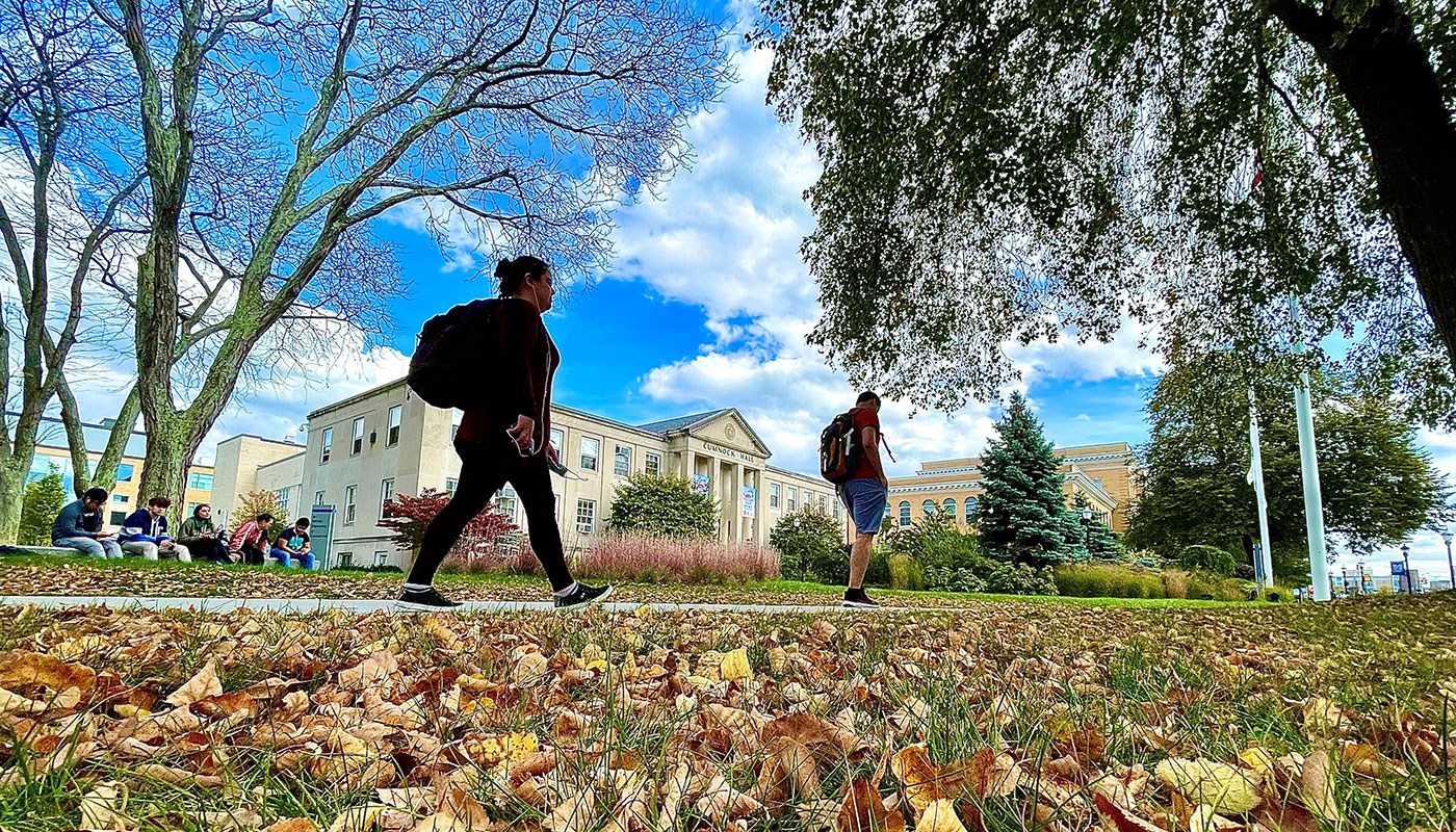 Students walk in front of Cumnock Hall on UMass Lowell's North Campus with fall leaves in foreground