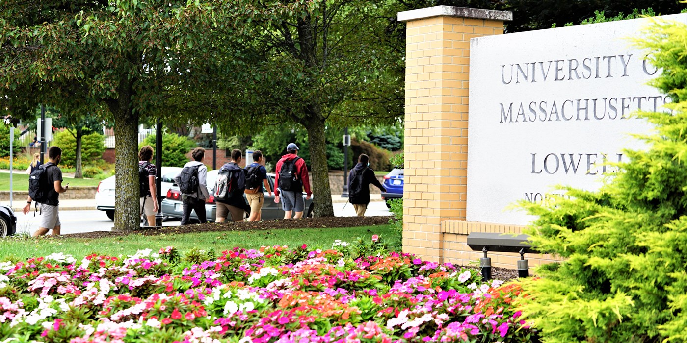 Students walking on north campus with flowers and University of Massachusetts Lowell sign in foreground