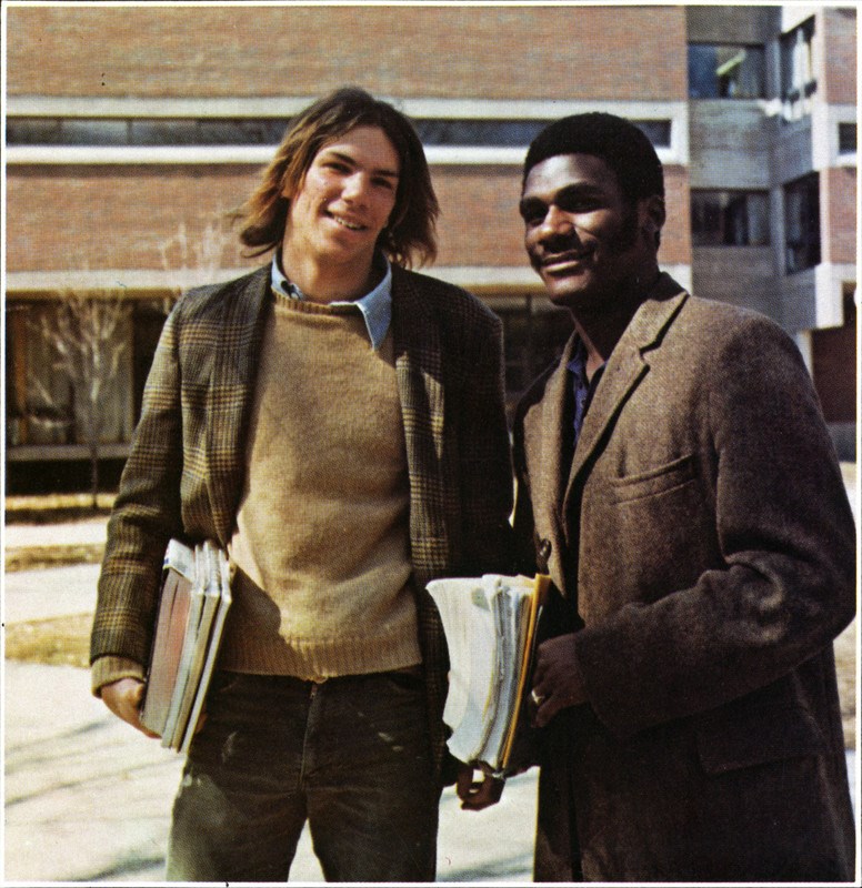 Two male students holding books outside of a building on UML's North Campus