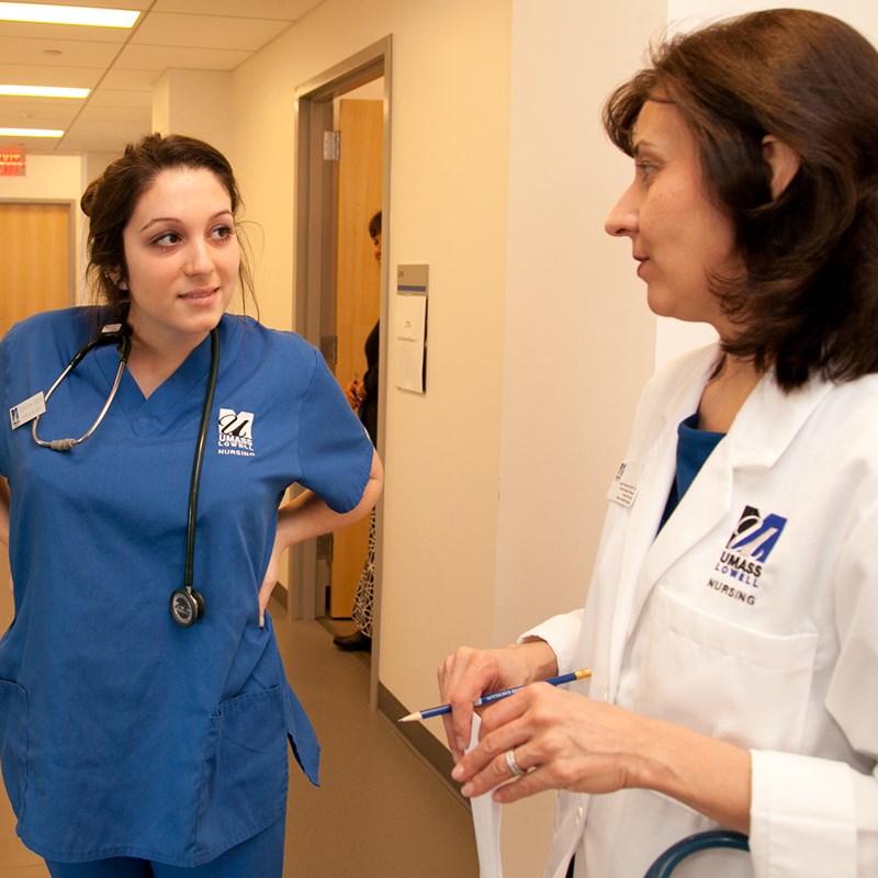 Female nursing student in scrubs speaks with female professor in white coat